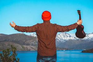 man met een gitaar op de achtergrond van bergen, bossen en meer foto