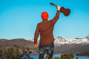 man met een gitaar op de achtergrond van bergen, bossen en meer foto