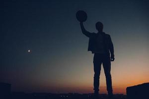 silhouet van het portret van een man met hoed die naar de zonsondergang over de stad kijkt foto