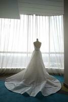 mooi wit bruiloft jurk Aan een wit mannequin in de kamer met groot venster foto