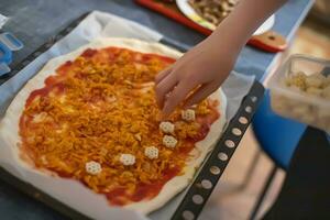 hand- toevoegen ingrediënten Aan eigengemaakt pizza. gemakkelijk voedsel gemaakt van goedkoop voedingsmiddelen. voorbereidingen treffen voedsel Bij huis. foto