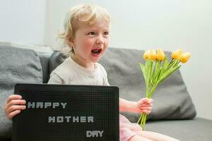 weinig meisje houdt een boeket van geel tulpen en een teken dat zegt gelukkig moeder dag. kind geeft bloemen naar moeder voor vakantie. foto