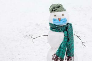 grappig sneeuwman in beschermend medisch masker Aan wit achtergrond. Kerstmis achtergrond gedurende coronavirus. foto