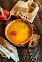 tomaat soep in een klei bord Aan een houten wijnoogst boerderij tafel in de buurt een stuk van bruin brood. foto