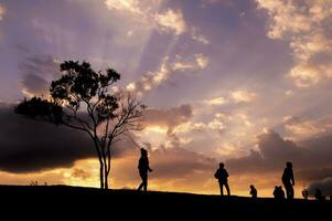 silhouet van mensen wandelen Aan de heuvel met dramatisch lucht foto