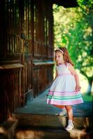 de meisje naar beneden de trap van een houten huis in de dorp. mooi houten deur in een oud huis. een kind in een mooi wit jurk wandelen in de straat. foto