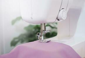 dichtbij omhoog van naaien machine werken met Purper kleding stof, steek nieuw kleding. foto