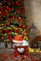 weinig verrast kind in de kerstman kostuum in feestelijk kamer Aan Kerstmis vooravond. meisje Aan achtergrond van Kerstmis boom. foto