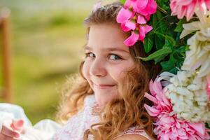 mooi weinig meisje van peuter- leeftijd in een delicaat jurk zittend Aan een schommel versierd met bloemen . foto