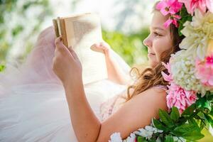 mooi meisje is aan het liegen Aan schommel met boek in handen. kind leest boeken in natuur. foto