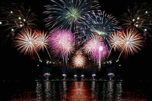 geweldig mooi kleurrijk vuurwerk op de feestavond, te zien op het zeestrand met veelkleurige reflectie op water foto