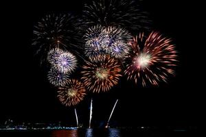 geweldig mooi kleurrijk vuurwerk op de feestavond, te zien op het zeestrand met veelkleurige reflectie op water foto