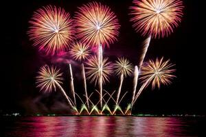 geweldig mooi kleurrijk vuurwerk op de feestavond, te zien op het zeestrand met veelkleurige reflectie op water foto