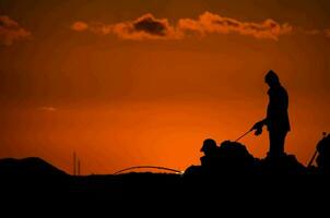 silhouet van een Mens visvangst Bij zonsondergang foto