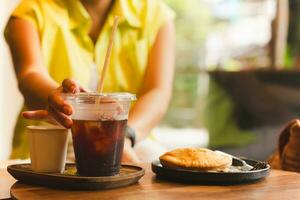 vrouw hand- bereiken glas van koffie Aan tafel. foto