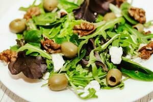 salade bladeren met rucola, kaas, groen olijven en noten in een bord, gezond eetpatroon salade foto