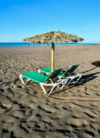 twee lounge stoelen en een paraplu Aan een zanderig strand foto