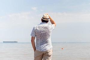 jonge man in zomerkleren staande op een pier, zee op de achtergrond foto