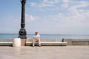 jonge man zittend op de bank bij de zee foto