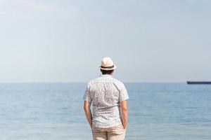 jonge man in zomerkleren staande op een pier, zee op de achtergrond foto