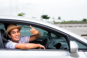 jonge aziatische man duim opdagen tijdens het autorijden. foto
