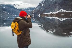 man die op de achtergrond van bergen en meer staat, maakt een foto