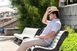 jonge kerel in de hoed zittend op een bankje in het park of in de zeehaven