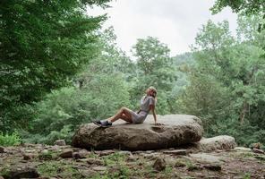 vrouw zittend op een grote rots in het bos, rusten of mediteren foto