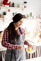 jonge latijnse vrouw die eieren zwaait die in de keuken koken foto