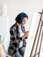 creatieve vrouw met blauw geverfd haar schilderij in haar atelier foto