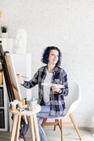 creatieve vrouw met blauw geverfd haar schilderij in haar atelier foto