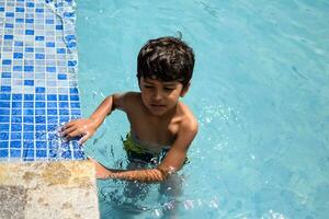 gelukkig Indisch jongen zwemmen in een zwembad, kind vervelend zwemmen kostuum langs met lucht buis gedurende heet zomer vakanties, kinderen jongen in groot zwemmen zwembad. foto