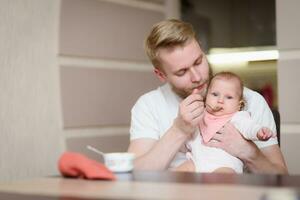 vader voeden zijn baby fruit puree in de keuken foto