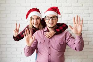 gelukkig Kerstmispaar in santahoeden op witte bakstenen muurachtergrond foto