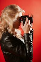 portret van een mooi vrouw fotograaf met een camera in haar handen wie is wezen gefotografeerd in een foto studio Aan een rood achtergrond