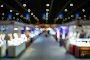 wazig afbeeldingen van handel beurzen in de groot hal. beeld van mensen wandelen Aan een handel eerlijk tentoonstelling of expo waar bedrijf mensen tonen innovatie werkzaamheid en Cadeau producten in een groot hal. foto