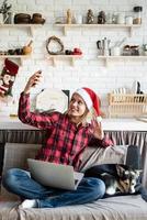 jonge vrouw in kerstmuts die haar vrienden begroet in videochat op laptop foto