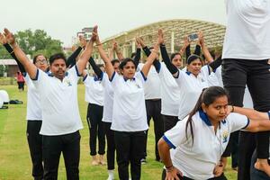 nieuw Delhi, Indië, juni 21, 2023 - groep yoga oefening sessie voor mensen Bij Yamuna sport- complex in Delhi Aan Internationale yoga dag, groot groep van volwassenen Bijwonen yoga klasse in krekel stadion foto