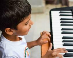 Aziatisch jongen spelen de synthesizer of piano. schattig weinig kind aan het leren hoe naar Speel piano. kind handen Aan de toetsenbord binnen. foto