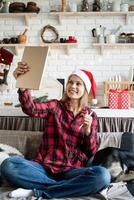 jonge blonde vrouw in kerstmuts bezig met tablet zittend op de bank foto