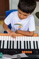 Aziatisch jongen spelen de synthesizer of piano. schattig weinig kind aan het leren hoe naar Speel piano. kind handen Aan de toetsenbord binnen. foto