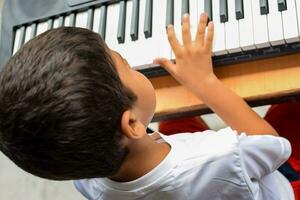 Aziatisch jongen spelen de synthesizer of piano. schattig weinig kind aan het leren hoe naar Speel piano. kind handen Aan de toetsenbord binnen. foto