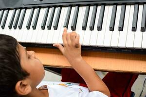 Aziatisch jongen spelen de synthesizer of piano. schattig weinig kind aan het leren hoe naar Speel piano. kind handen Aan de toetsenbord binnen. foto