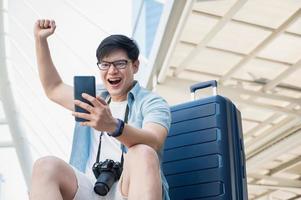 Aziatische reiziger man is blij terwijl hij naar smartphone kijkt