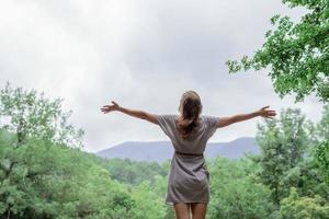 jonge vrouw die op een grote rots in het bos staat en wegkijkt foto