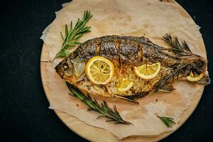gebakken vis in oven met citroen en rozemarijn gelegd uit snijdend bord en perkament papier.op donker achtergrond. foto
