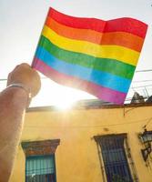 een hand houdt een regenboogvlag van de lgbtq-beweging vast, huis op de achtergrond foto