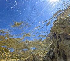 onderwater- beeld van een rotsachtig kustlijn met turkoois water naar de oppervlakte foto