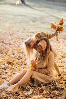 moeder en haar dochter zitten en hebben plezier in het herfstpark. foto