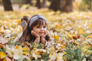 mooi klein meisje ligt tussen de gele bladeren in het herfstpark foto